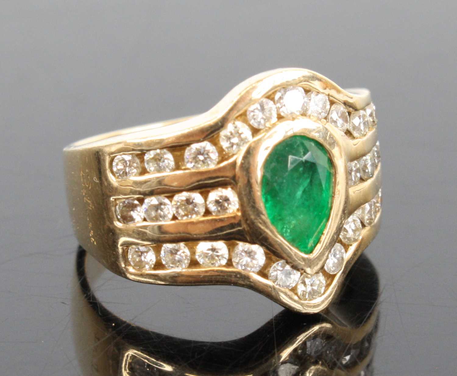 A 14ct yellow gold emerald and diamond dress ring, featuring a centre pear cut emerald in a bezel