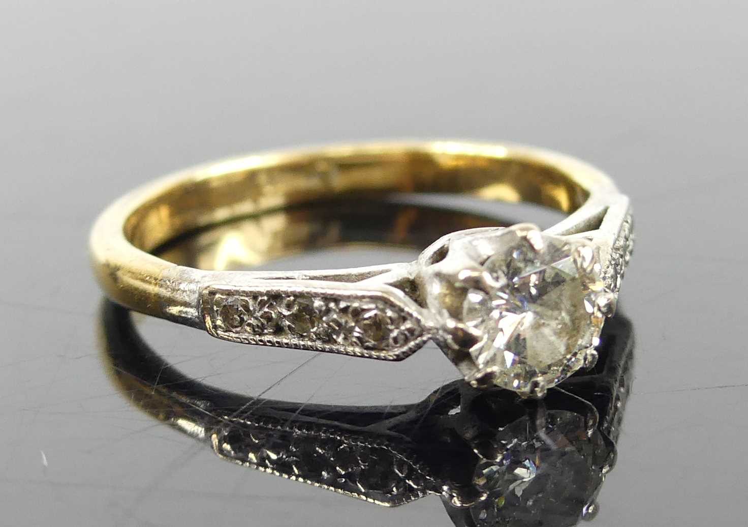 A yellow and white metal, diamond solitaire ring, featuring a round brilliant cut diamond in an