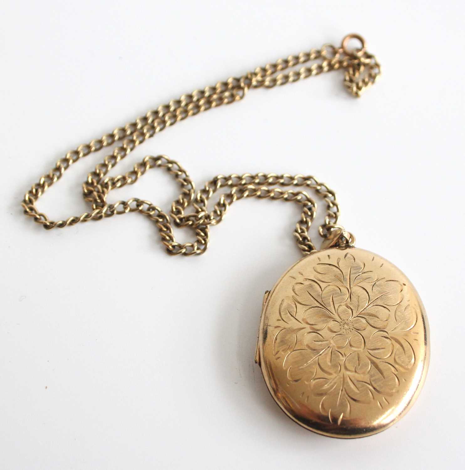 A 9ct yellow gold oval locket, engraved with a floral pattern to the front, attached to an open