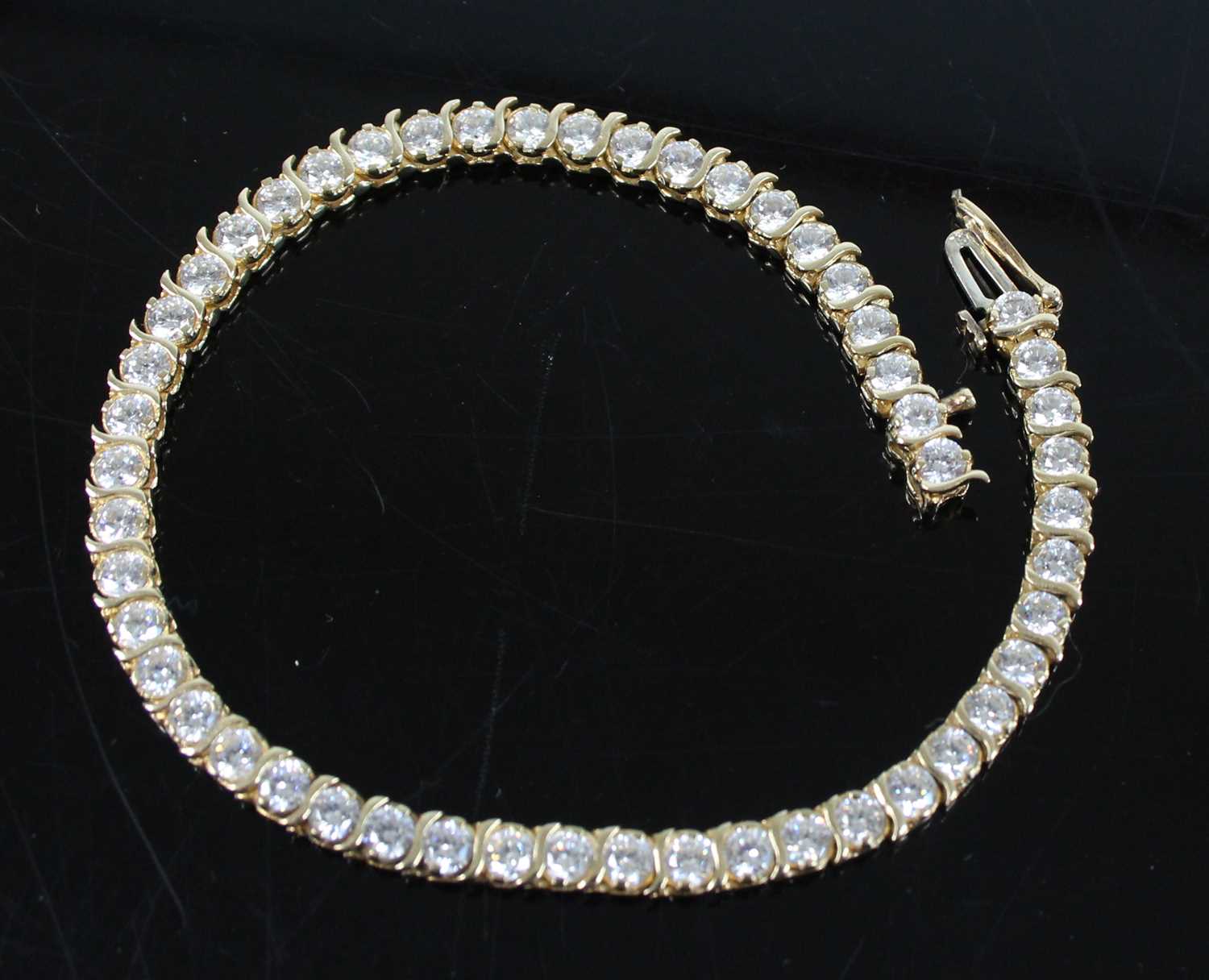 A yellow metal cubic zirconia tennis bracelet, featuring fifty-one 3 x 1.9mm round cubic zirconia in