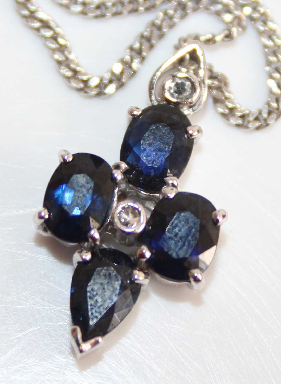 A white metal, sapphire and diamond point set pendant, arranged as two oval and two pear cut