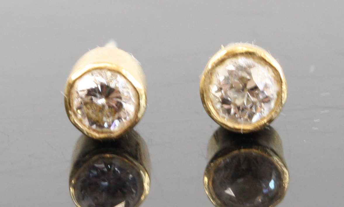 A pair of yellow metal diamond ear studs, the bezel set round cut diamonds each dia. approx 3.6mm