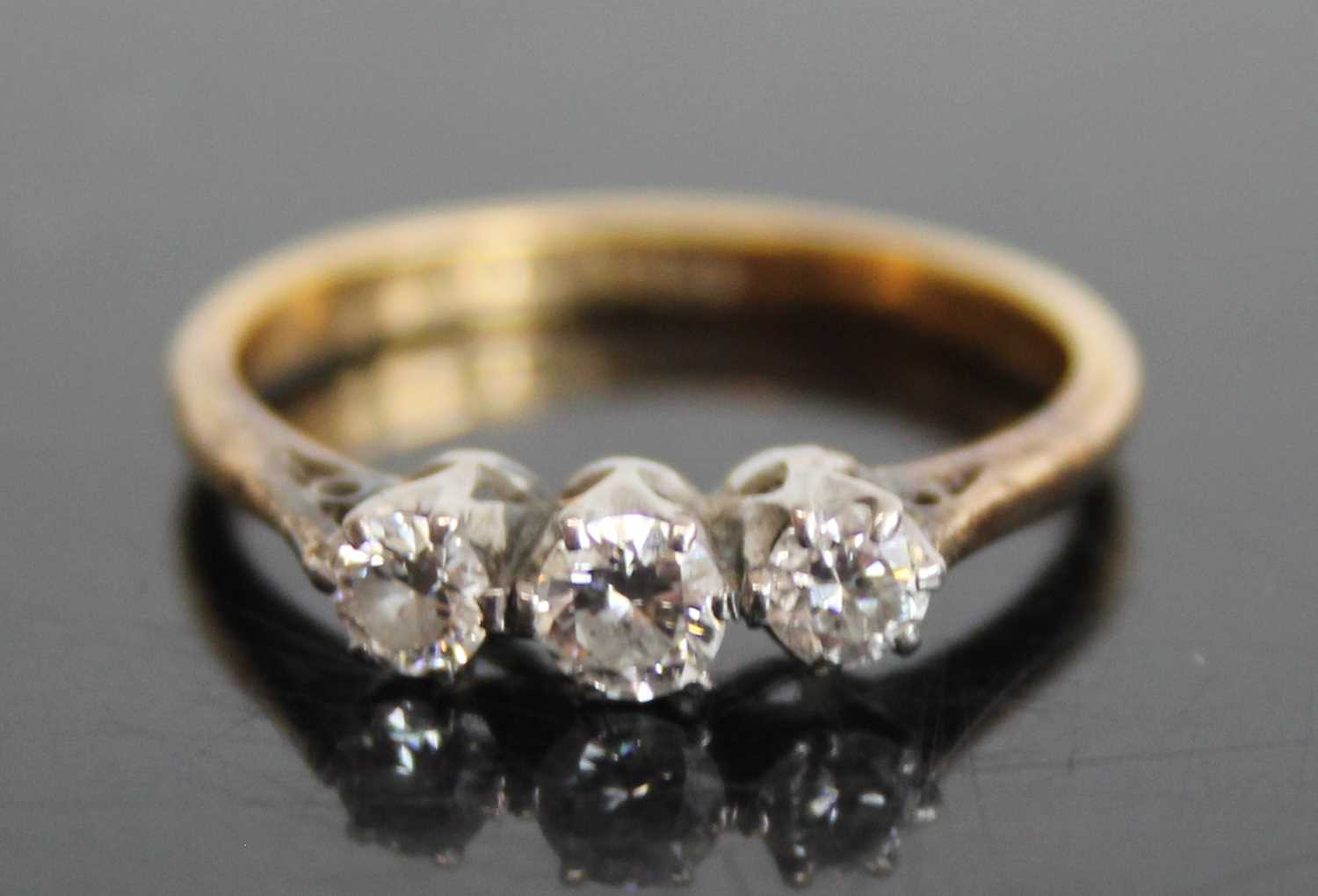 An 18ct gold and platinum diamond trilogy ring, arranged as three claw set round cuts in a line