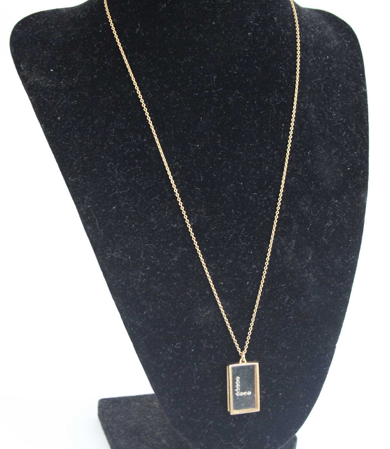 A yellow metal rectangular glass pendant with 8 1.5mm single cut white stones in a letter L shape