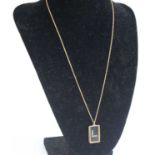 A yellow metal rectangular glass pendant with 8 1.5mm single cut white stones in a letter L shape