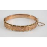 An Edwardian 9ct gold hinged hollow bangle, one side having engraved scroll leaf decoration within a