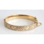 A 9ct yellow gold oval hinged hollow bangle, half engraved with scrollwork detail, with a box