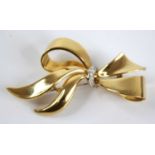 A modern 18ct gold and diamond point set ribbon brooch, being centre set with row of five small pavé