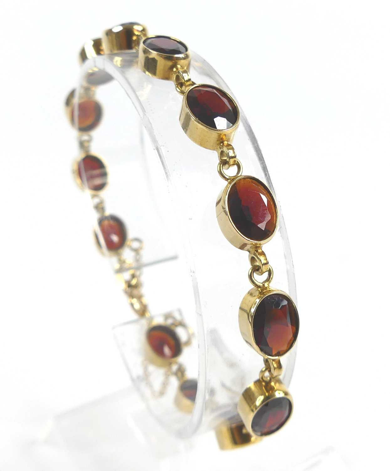 A 9ct yellow gold garnet bracelet, comprising 13 oval almandine garnets in bezel settings, with bolt