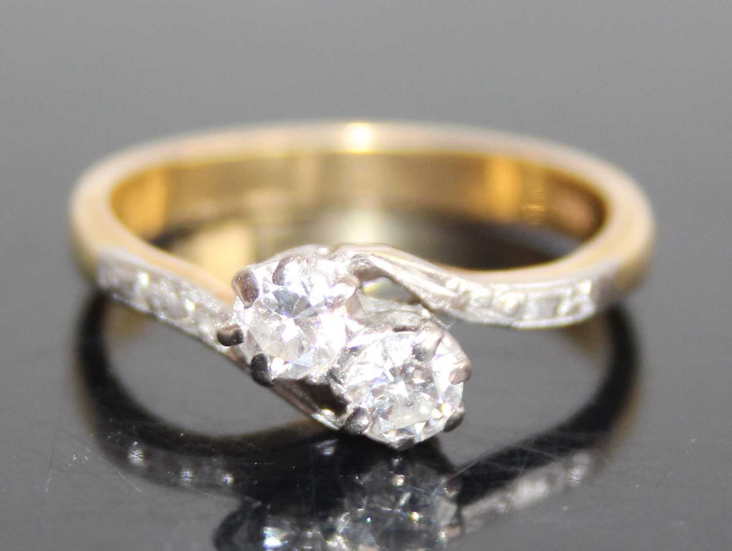 An 18ct gold diamond crossover ring, arranged as two claw set round cut diamonds, total diamond