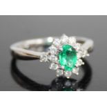 A contemporary 14ct white gold, emerald and diamond cluster ring, the four-claw set oval cut emerald