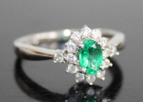A contemporary 14ct white gold, emerald and diamond cluster ring, the four-claw set oval cut emerald