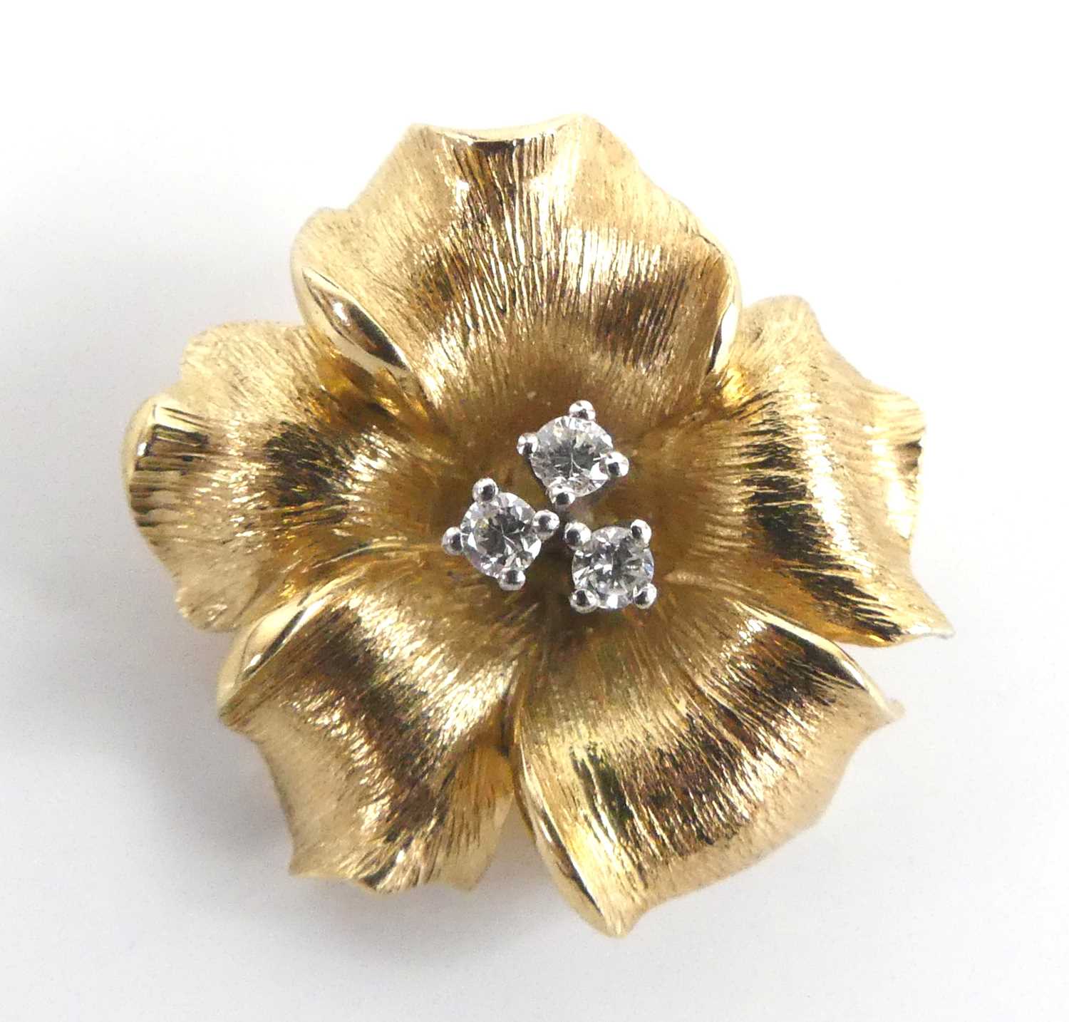 A yellow metal diamond set stylised flower brooch, featuring three round brilliant cut diamonds claw