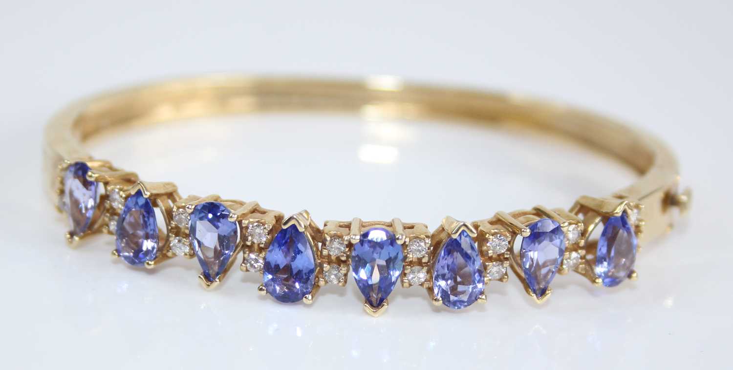A contemporary yellow metal, tanzanite and diamond set hinged bangle, arranged as eight pear cut