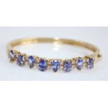 A contemporary yellow metal, tanzanite and diamond set hinged bangle, arranged as eight pear cut