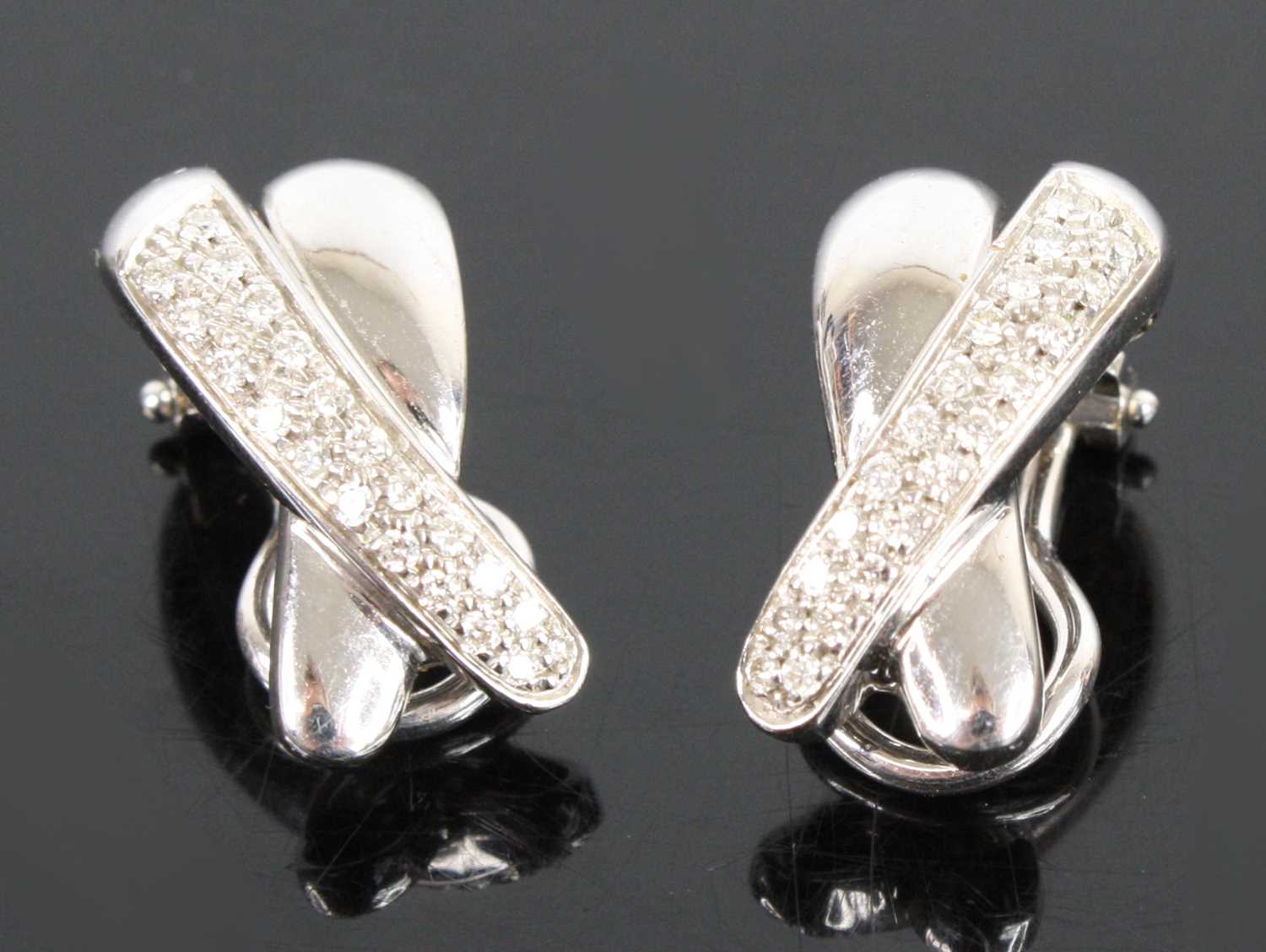 A pair of 18ct white gold diamond two-strand crossover clip earrings, each comprising a strand of 21