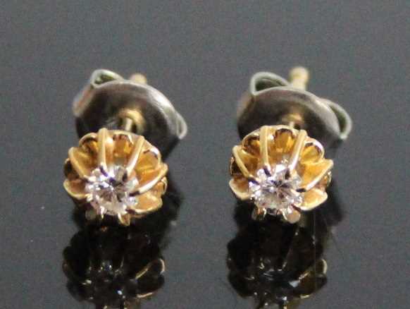 A pair of yellow metal diamond stud earrings, each with a round brilliant cut diamond in a heavy