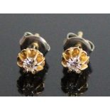 A pair of yellow metal diamond stud earrings, each with a round brilliant cut diamond in a heavy