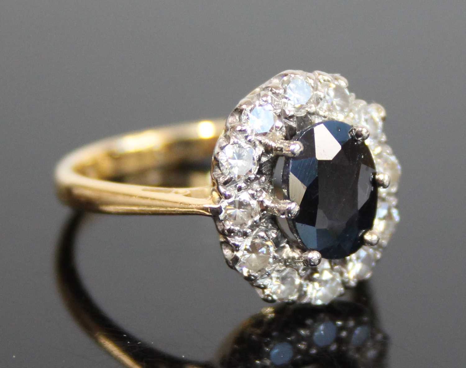 A yellow and white metal, sapphire and diamond oval cluster ring, the centre sapphire within a