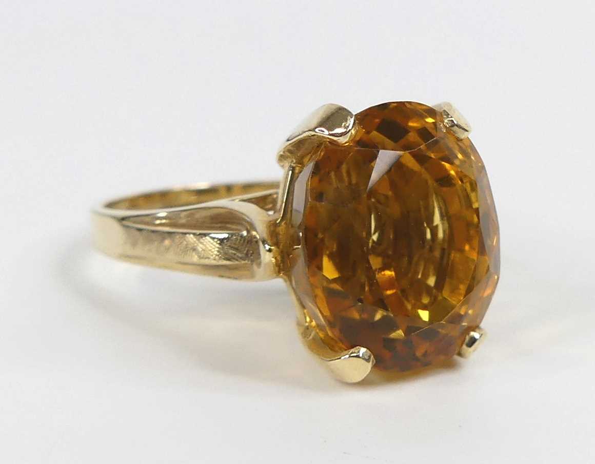 A yellow metal citrine single stone ring, featuring an oval citrine in a four-claw setting with