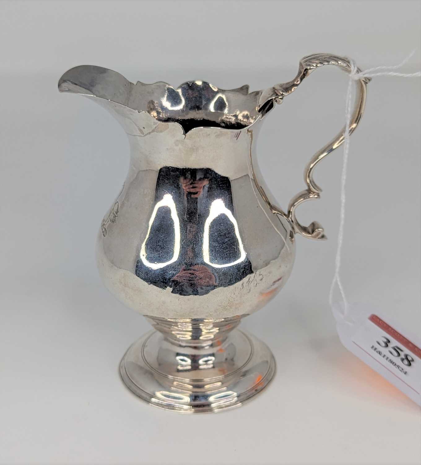 An 18th century silver cream jug of helmet shape having a everted rim, flying C-scroll handle on