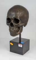 A bronzed metal model of a skull, mounted upon a polished black hardstone plinth, height 35cm