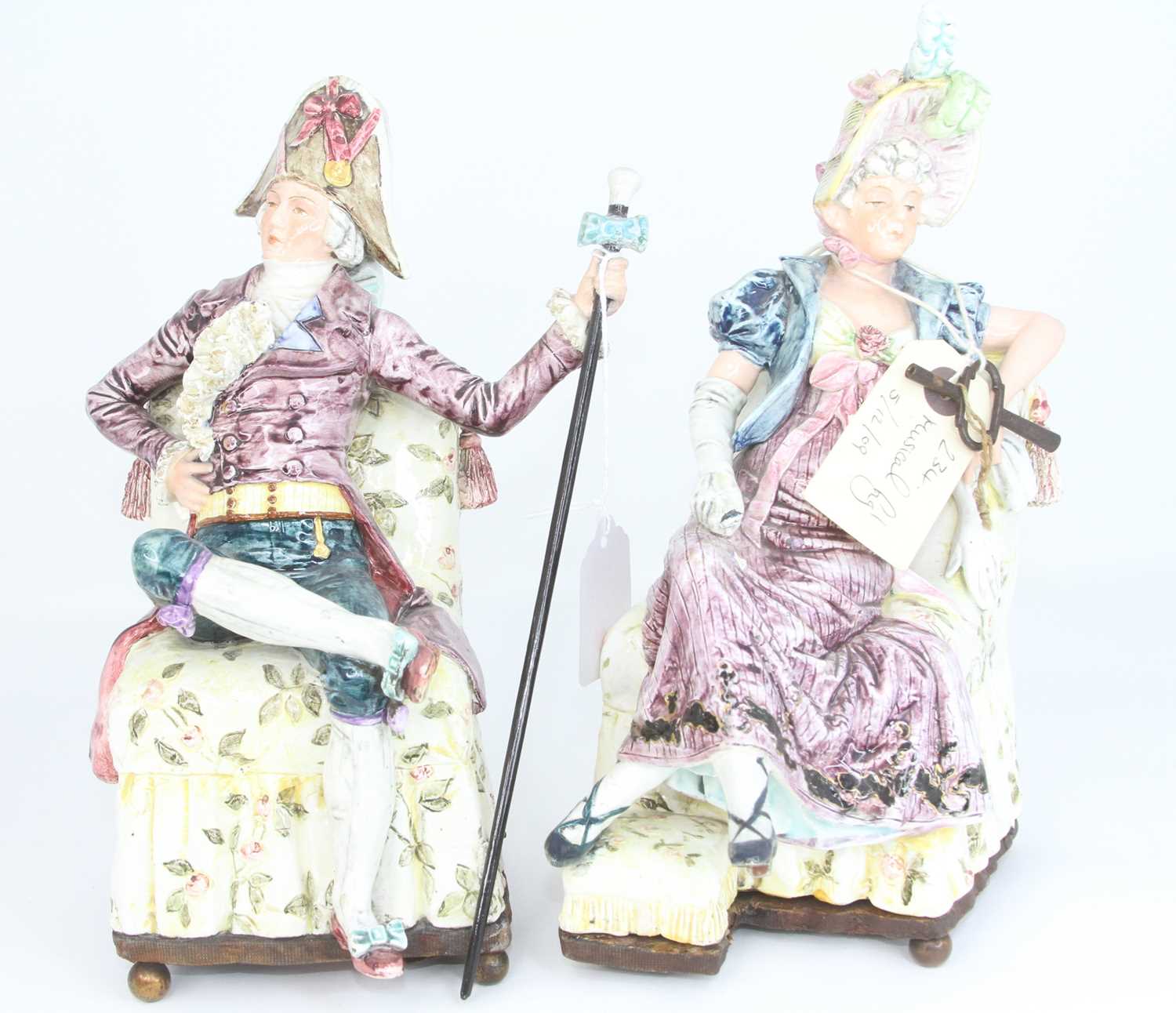 A pair of continental pottery figures, each shown reclining in 18th century dress, largest height