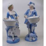 A pair of porcelain figures of a gentleman and lady, each shown standing holding a basket, height