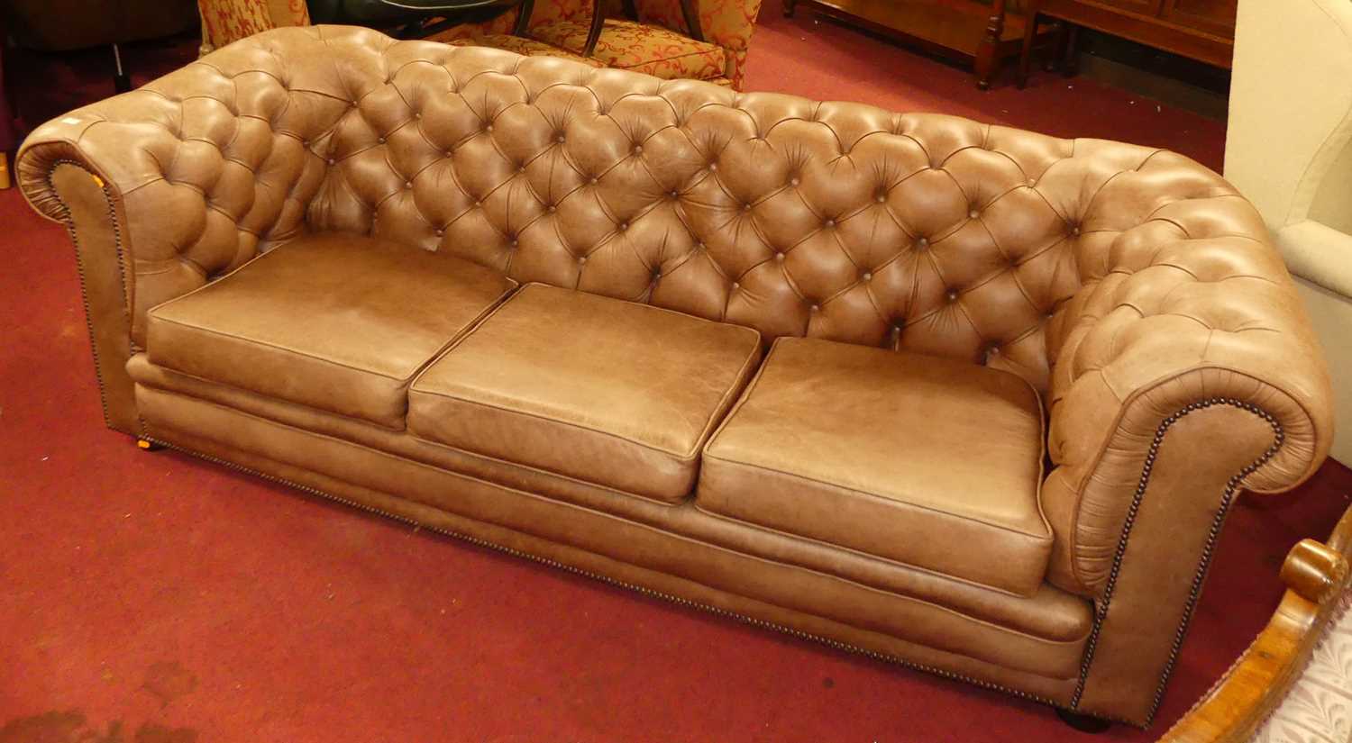 A contemporary tan leather buttoned upholstered three-seater Chesterfield, having squab cushions,