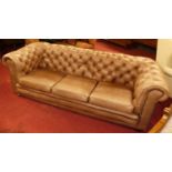 A contemporary tan leather buttoned upholstered three-seater Chesterfield, having squab cushions,