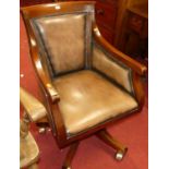 A contemporary mahogany tan leather and further studded swivel desk chair, raised on roller castors,