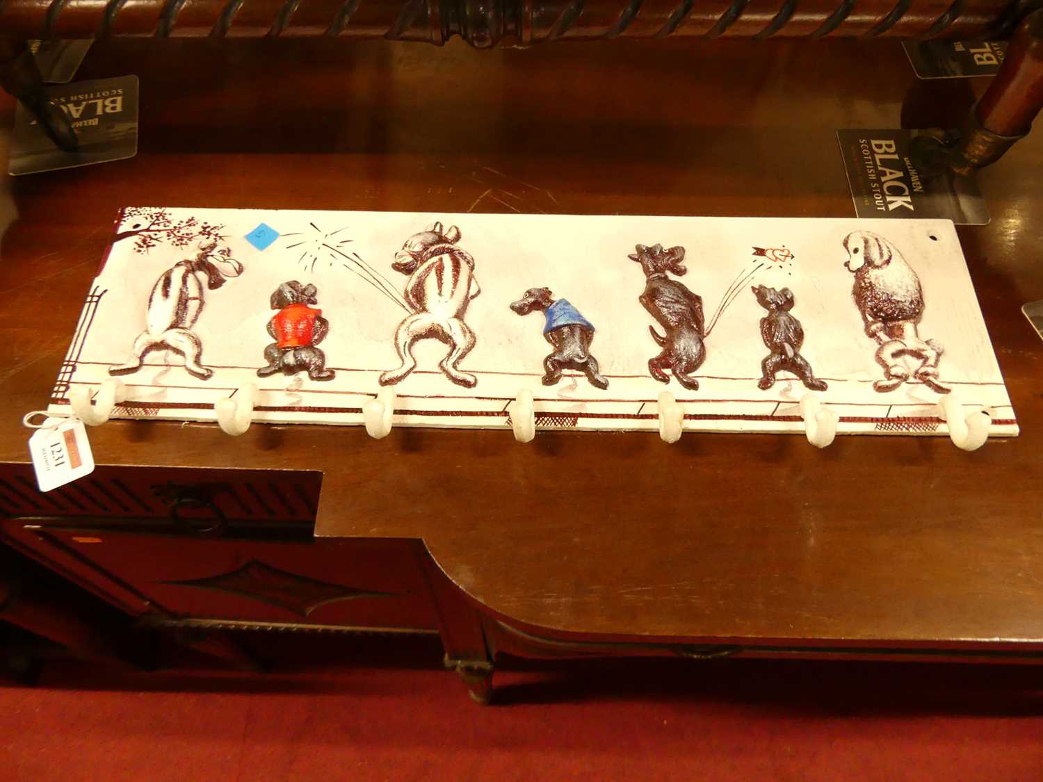 A contemporary painted cast metal wall mounted set of seven hat-hooks, displaying novelty peeing