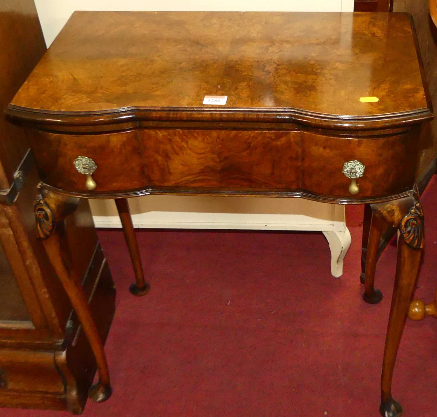 A 1930s figured walnut serpentine single drawer side table, raised on shell capped cabriole