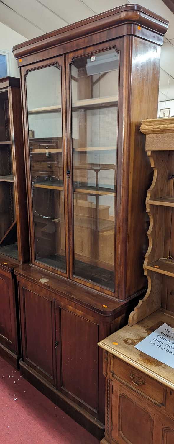 A mid-Victorian narrow mahogany round cornered bookcase cupboard, having twin glazed upper doors