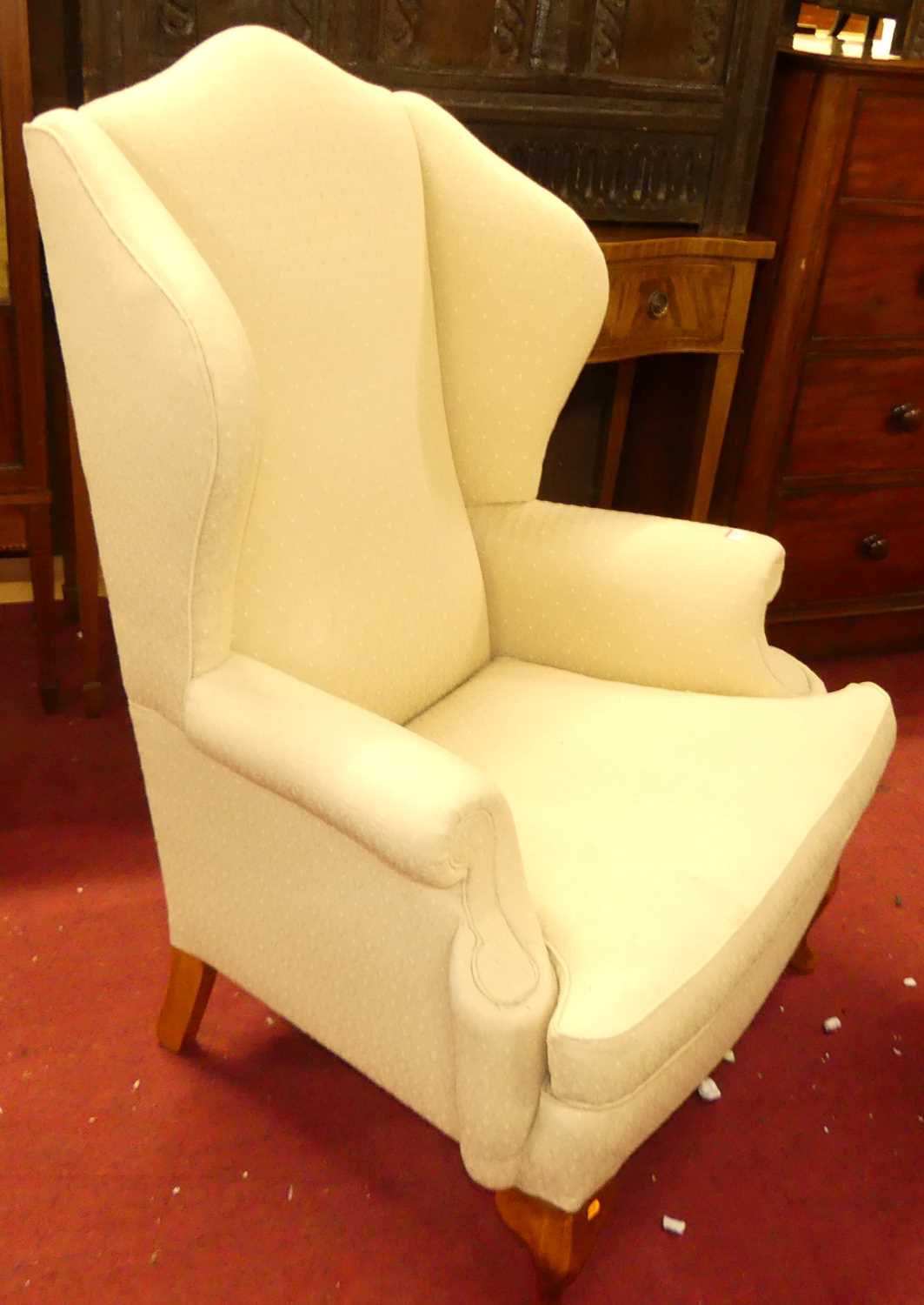A contemporary cream floral fabric upholstered wingback scroll armchair, having squab cushion and