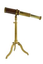 A reproduction three-draw brass and hardwood telescope on an adjustable folding brass tripod base,