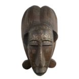 A Central African Punu style mask in carved wood with applied metal, the later tooled in depiction