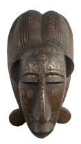 A Central African Punu style mask in carved wood with applied metal, the later tooled in depiction