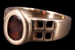 A contemporary Macintosh-influenced garnet finger ring, having an oval of approximately one carat