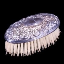 A 1950s silver-backed hair brush, decorated with embossed foliate scrolls centred by a vacant