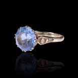 A 1970s aquamarine-coloured paste solitaire ring, the 11 mm round-cut stone claw-set between the