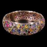 An impressive tutti frutti multi-gem-set 9 ct gold hinged bangle, comprising an open, dense and