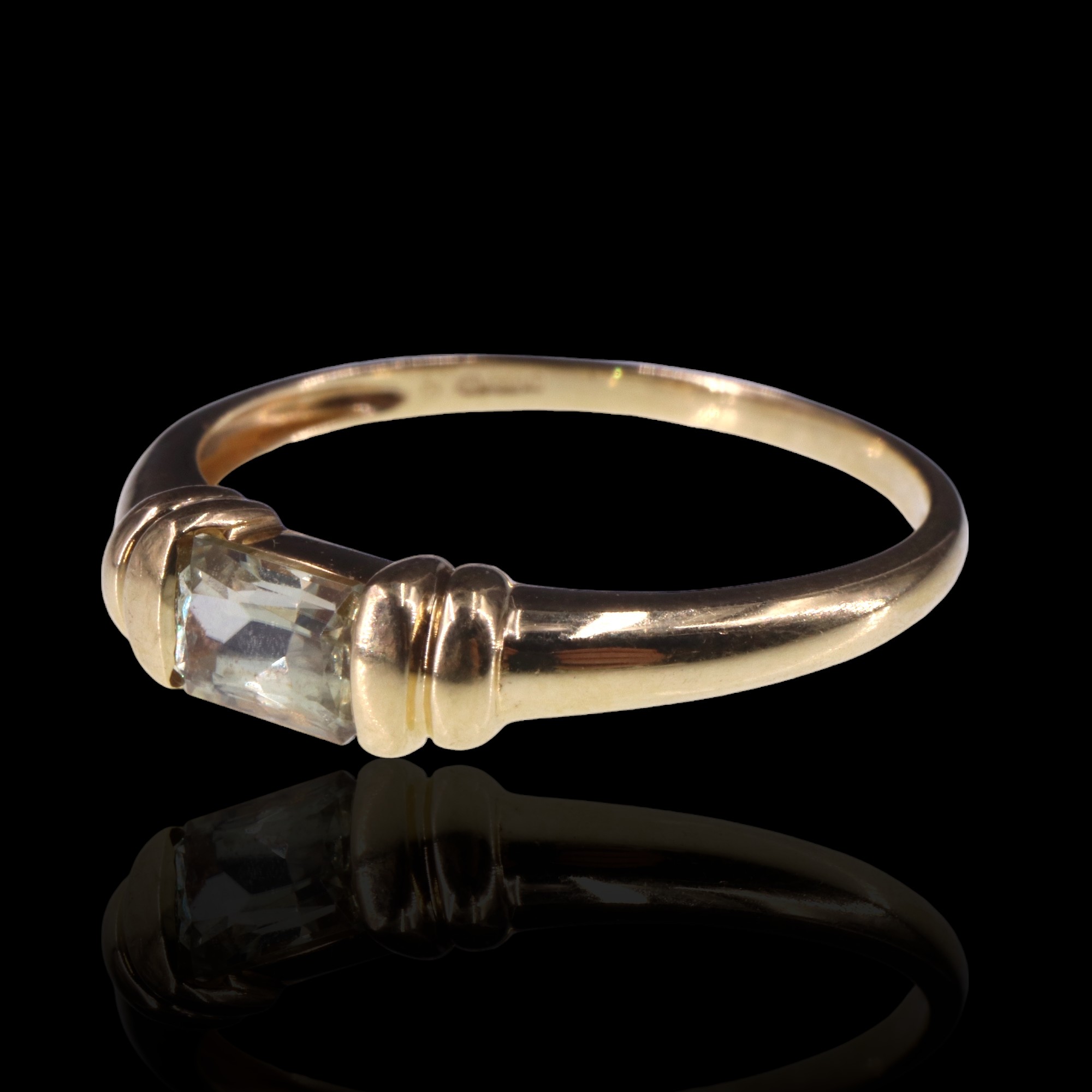 A pale yellow topaz finger ring, the emerald cut stone clinched between paired collars on an 18 ct