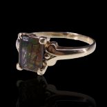 An ammolite ring, comprising a rectangular shallow cabochon, claw-set between the scroll shoulders