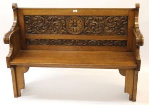 Late 19th Century oak settle, the floral carved panel back above a plank seat and shaped end