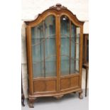 Early 20th Century walnut bow fronted display cabinet, the shell carved moulded cornice above two