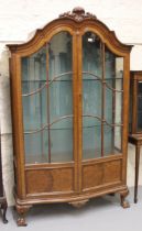 Early 20th Century walnut bow fronted display cabinet, the shell carved moulded cornice above two