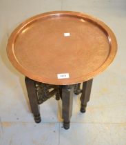 Small Middle Eastern circular copper tray with engraved decoration on a folding wooden stand, 42cm