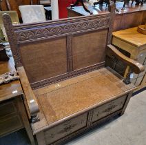 A 19th century oak carved settle, the hinged seat opening to a storage compartment.