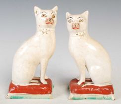A pair of 19th century Staffordshire pottery cats, seated on red painted cushions with green and